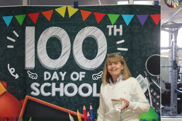 teacher posing in front of 100th day banner